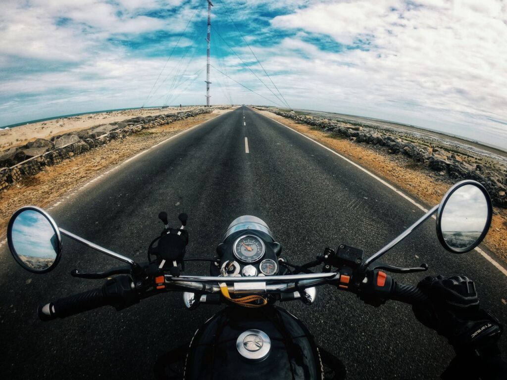 From above of crop unrecognizable person in gloves driving modern motorbike on empty asphalt road near grassland in countryside